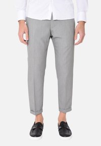 Pantaloni eleganti grigi, a taglio affusolato, realizzati in tessuto leggero. Presentano una sottile trama e risvolti sui polsini. Abbinati a scarpe nere senza lacci.