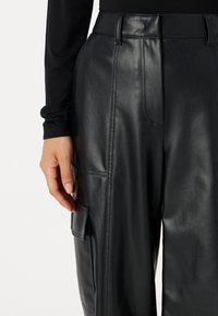 Black leather trousers featuring a high waist, side pockets, and a patch pocket on the thigh. The surface has a smooth, glossy texture.