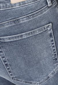Vaqueros de mezclilla azul oscuro con un bolsillo trasero que presenta sutiles detalles de costura y una textura suave.