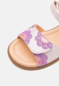 Rosa sandaler med en glitrende lilla bølgete stropp, borrelås og en glatt beige fotseng med en brun gummisåle.