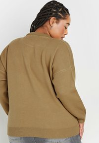 Übergroßer khakifarbenes Strickpullover mit strukturiertem Oberflächen, gerippten Bündchen und einem runden Ausschnitt. Das gesamte Stück ist minimalistisch im Design.