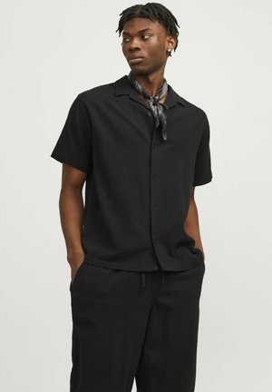 Camisa negra de manga corta en un tejido texturizado, con un cierre de botones en la parte delantera y cuello. Combinada con pantalones a juego para un look cohesivo.