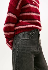 Röd och rosa randig stickad tröja med en strukturerad yta, ihop med högmidjade svarta jeans som har en liten logotyp på fickan.