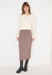 Un pull en tricot léger crème associé à une jupe en laine marron de longueur cuisse. Des bottes de combat noires à lacets. Design simple et ajusté avec des accents côtelés.