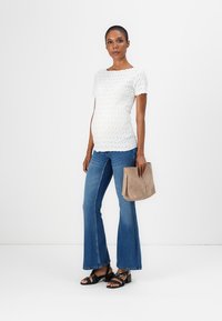 Hvit teksturert kortermet topp, blå vide jeans, svarte sandal med stropper og beige veske. Antrekket er uformelt og tilpasset for å romme en mage.