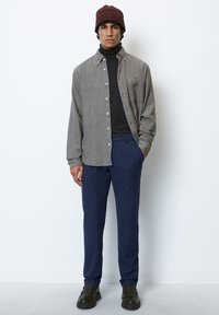 Gray button-up shirt over a black turtleneck, paired with textured navy pants and black shoes. Includes a dark brown beanie.