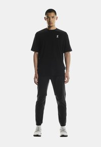 Fekete, rövid ujjú póló, kis fehér logóval, fekete szűkített nadrággal és fehér sportcipővel párosítva. Egyszerű, testhezálló dizájn.