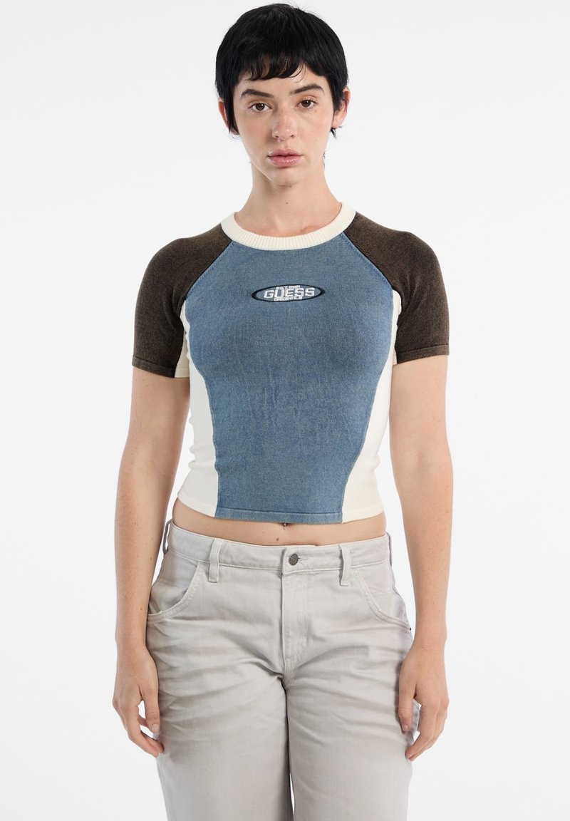 Top corto a maniche corte con davanti in denim blu, maniche marroni e corpo color crema. Presenta un logo al centro.