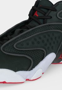 Μαύρο και κόκκινο αθλητικό παπούτσι με διάτρητο πλαϊνό πάνελ, μαύρα κορδόνια και λευκή ενδιάμεση σόλα με κόκκινη εξωτερική σόλα και λογότυπο Jumpman.