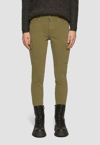 Cargo-broek in olijfgroene stof, met zijzakken, slim fit en versterkte stiksels. Gecombineerd met zwarte veterschoenen voor in de strijd.