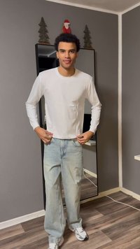 Vit långärmad tröja med rund halsringning, kombinerad med ljusblåa, löst sittande jeans och vita och svarta sneakers. Reflekterande spegel i bakgrunden.