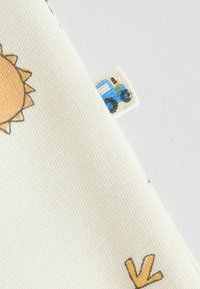 Krémszínű háttérrel rendelkező pamut anyag nap- és traktorillusztrációkkal. Puha tapintású, élénk, egyszerű sárga és kék mintákkal.