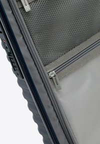 Valigia da viaggio grigia con una superficie testurizzata, dotata di una tasca in rete, doppi zip e un pannello di lucchetto digitale sul lato.
