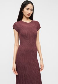 Πλεκτό φόρεμα με ρίγες σε βαθύ μπορντό, με κοντά μανίκια, εφαρμοστή γραμμή και ομαλή υφή. Διαθέτει λαιμόκοψη τύπου crew και μήκος μέχρι τον αστράγαλο.
