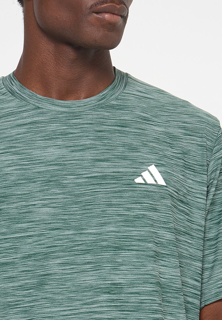 Camiseta deportiva verde hecha de tela texturizada, con un cuello redondo y un logo blanco de Adidas en un diseño triangular en el pecho.