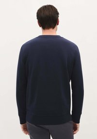 Granatowy sweatshirt z długimi rękawami, prążkowanym dekoltem i dołem, wykonany z miękkiego materiału o teksturowanym wyglądzie. Bez widocznych logo.