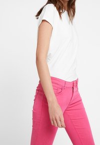 Vit kortärmad t-shirt i kombination med livfulla rosa slim-fit jeans med dragkedja och knappstängning, vilket framhäver en åtsittande siluett.