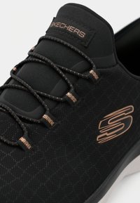 Μαύρο παπούτσι Skechers με υφή στην επιφάνεια, ελαστικά κορδόνια, μεταλλικές λεπτομέρειες και λευκή σόλα. Διαθέτει λογότυπο στο πλάι.