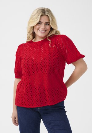 Rode blouse met korte mouwen en een chevron uitgesneden patroon, ronde halslijn en licht opgeblazen mouwen, gecombineerd met donkerblauwe jeans.