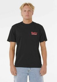 Black cotton t-shirt with short sleeves, featuring a small red graphic logo on the left chest. Worn with light blue denim jeans.