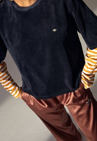 Mörkblå sammet långärmad topp med randiga underärmar i orange och vitt, matchad med bruna satinsbyxor med logotypbroderi.