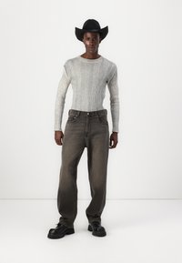 Grå ribbet genser med lange ermer, mørkegrå løse jeans og svart cowboyhatt med bred skygge, kombinert med kraftige svarte støvler.
