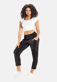 Hvid crop top med rund halsudskæring, parret med sorte satin joggerbukser med sidelommer og en glat tekstur. Hvide sneakers.