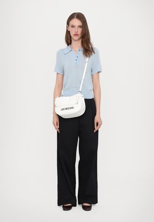 Weiße Umhängetasche mit floralen Akzenten und "LOVE MOSCHINO"-Logo. Das Modell trägt ein hellblaues Hemd mit Kragen und lockere schwarze Hosen.