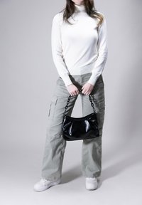 Black patent leather handbag with a chain handle, held in hands. The outfit includes a white turtleneck and light green cargo pants.