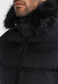 Black puffer jacket with a thick faux fur collar, featuring a zip closure, and quilted texture. The fabric has a smooth finish.