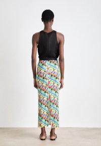 Top sin mangas negro combinado con una falda maxi de estampado colorido que presenta tonos vibrantes y una abertura en la parte trasera. El material parece ligero.