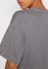 Přesměrný šedý tričko s texturovaným povrchem, s vybledlým vzorem a krátkými rukávy. Výstřih je měkký a žebrovaný.