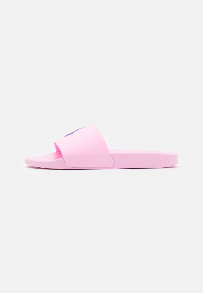 Sandale rose glissière avec une large sangle et une semelle plate sur un fond uni gris clair, vue de profil.