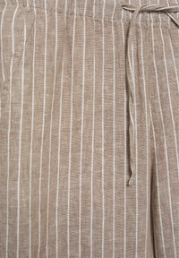 Tissu en lin beige avec de fines rayures blanches verticales et un cordon noué à la taille élastique d’un vêtement.