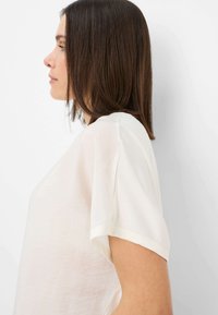 Hvid kortærmet bluse med en afslappet pasform, der har en rund halsudskæring og blødt, let væv. Minimalistisk design, glat tekstur.