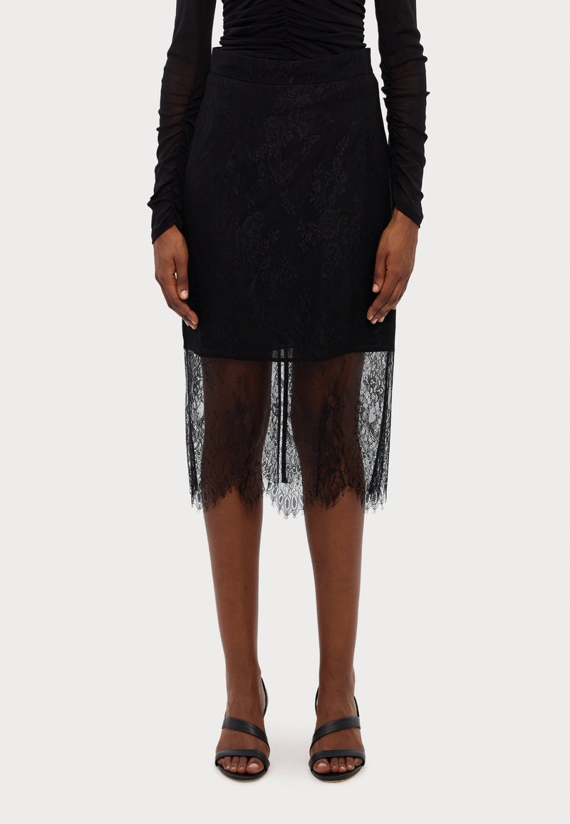 Black lace skirt featuring a fitted upper layer and sheer lace hem with scalloped edges. Worn with black strappy high heels.