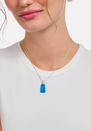 Blue gummy bear pendant on a silver chain, showcased on a white shirt. The pendant features a smooth, glossy texture.