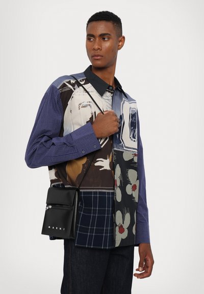 Patchwork shirt with varying patterns in blue, black, and cream, featuring a collar and button details. Black crossbody bag with logo.