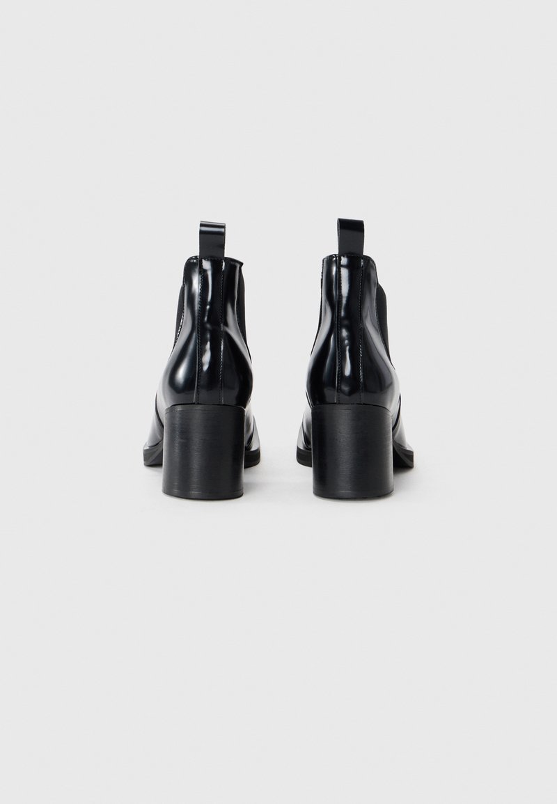 Bottines en cuir verni noir avec un bout rond, une texture lisse, des talons carrés de hauteur intermédiaire et des languettes à l'arrière pour un enfilage facile.