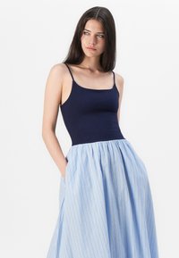 Top navy ajustado con tirantes finos, combinado con una falda azul a rayas con diseño plisado y bolsillos.