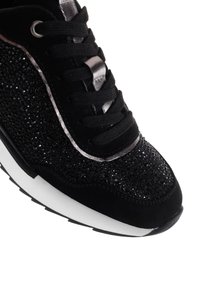 Sneaker nera con tomaia in tessuto luccicante, accenti in suede, dettagli metallici, lacci neri e suola intermedia bianca. Presenta una superficie testurizzata.