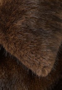 Brązowa tekstura futra o zróżnicowanej długości, wykazująca miękki wygląd. Włókna są gęste i wydają się jedwabiste, ukazując naturalne wariacje kolorystyczne.