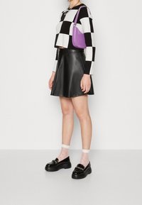 Pull court à manches longues à carreaux noir et blanc, associé à une jupe évasée en cuir noir, un sac à main lavande et des mocassins noirs épais.