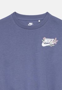 T-shirt blu a girocollo con logo Nike bianco e design floreale in rosa e verde sulla parte superiore sinistra del petto.