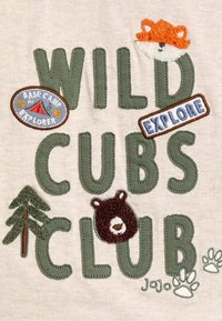 Groene geborduurde letters die "WILD CUBS CLUB" spellen op een beige stof. Kenmerkt een vos, een beer, boompatches en pootafdrukken. Getextureerde stitchingdetails.