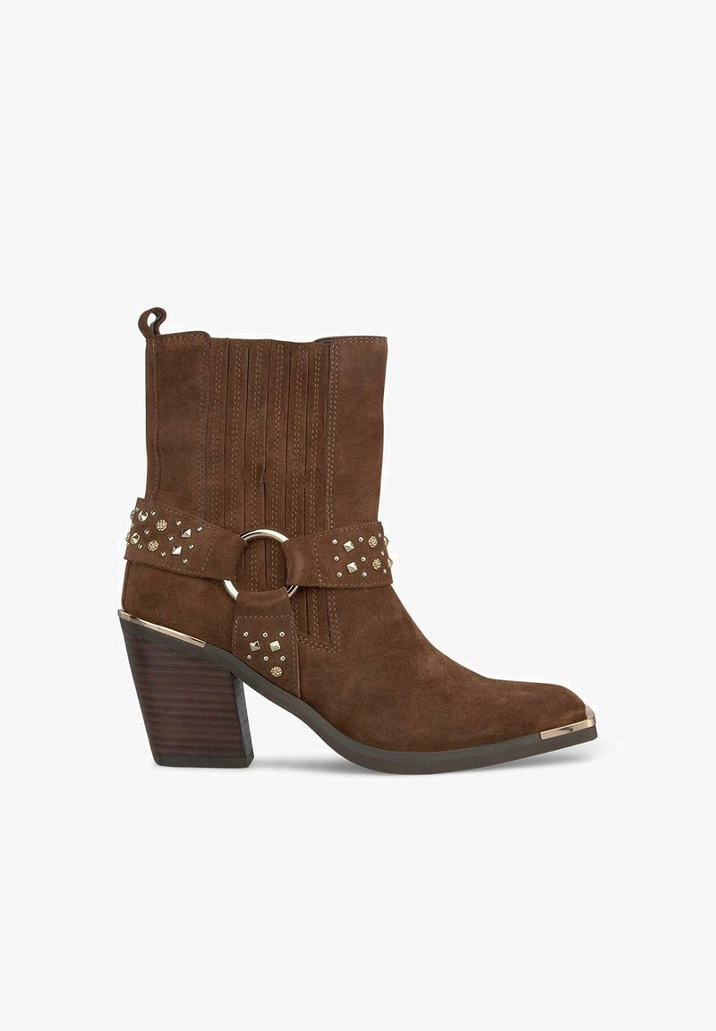 Bottines en daim marron avec un bout pointu, des sangles décoratives, des clous et un talon épais au texture boisée. Présente des coutures verticales.