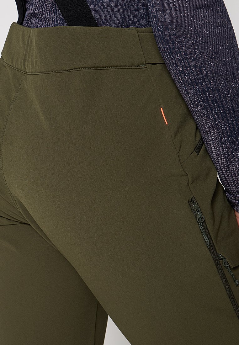Olivgrüne Sporthosen mit glatter Textur, ausgestattet mit seitlichen Reißverschlusstaschen und einer orangefarbenen Akzentnaht in der Nähe des Taillenbundes.