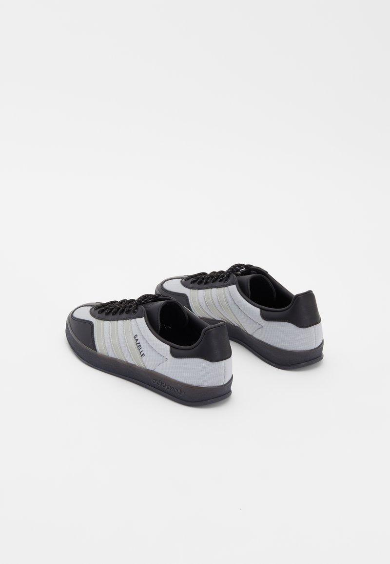 Graue und schwarze Turnschuhe mit einem strukturierten Obermaterial, drei horizontalen weißen Streifen, schwarzen Schnürsenkeln und einer Gummisohle.