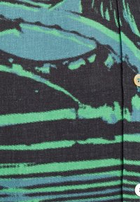 Korte mouwen shirt van zwarte stof met groene en blauwe abstracte strepen. Heeft een subtiele textuur en ronde knopen voor de sluiting.