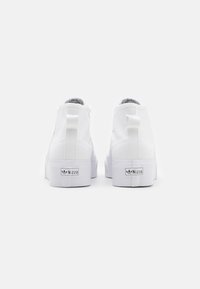 Zapatillas altas blancas con parte superior de lona, paneles laterales texturizados, suela de goma y detalle del logo en el talón.